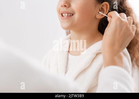 Glückliche Mutter, die im Badezimmer das Ohr der Tochter putzt Stockfoto