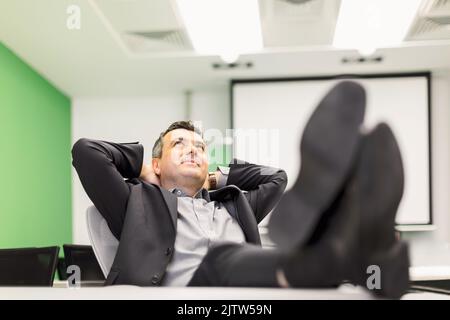 Entspannter, glücklicher Geschäftsmann mit Füßen auf dem Schreibtisch im Büro. Männliches Modell. Stockfoto