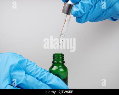 Ein Arzt in Handschuhen hält eine Pipette und eine Flasche Medizin in den Händen. Stockfoto