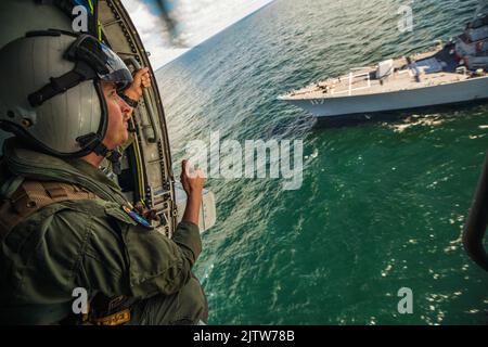 220830-N-GF955-2018 OSTSEE (AUG 30, 2022) U.S. Naval Aircrewman (Hubschrauber) 1. Class Russell Akers, von Charleston, S.C., Wellen zum Arleigh Burke-Klasse Lenkflugkörper-Zerstörer USS Paul Ignatius von einem MH-60R Sea Hawk Hubschrauber, zugewiesen zu Helicopter Maritime Strike Squadron (HSM) 79, Ablösung 2, Nach Abschluss einer Manövrierübung mit der Kearsarge Amphibious Ready Group und der schwedischen Marine, 30. August 2022. Paul Ignatius ist Teil der Kearsarge Amphibious Ready Group und startete 22. Marine Expeditionary Unit unter dem Kommando und der Kontrolle der Task Force 61/2 auf einem sc Stockfoto