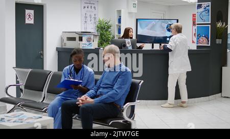 Asiatischer Rezeptionist, der am Empfangstresen des Krankenhauses arbeitet und dem Arzt bei Terminen und Patienten hilft. Medizinisches Personal, das Gesundheitskonsultationen und Kontrollbesuche im Wartebereich vorbereitet. Stockfoto