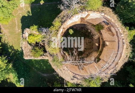 Blick von oben auf das verlassene Kircheninnere durch den dachlosen beschädigten Turm. Alte Tempelruinen im Grasfeld mit Bäumen. Horizontale Aufnahme. Hochwertige Fotos Stockfoto