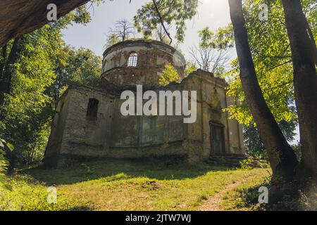 Beschädigte freiliegende Ziegelfassade einer verlassenen Kirche mit Turm und ohne Dach im grünen Wald. Alte christliche Architektur. Lubycza Krolewska. Horizontale Aufnahme. Hochwertige Fotos Stockfoto