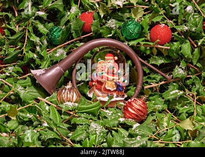 Nahaufnahme einer Weihnachtsmann-Schneekugel und eines Fuchses auf der Jagd nach Trompete oder Bügeln. In Stechpalme mit Schnee. Dies würde eine schöne Weihnachtskarte machen. Stockfoto