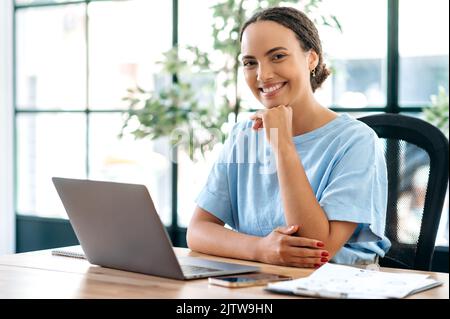 Hübsche, freundliche junge, gemischte Rasse, junge Frau, Geschäftsmentorin, Finanzberaterin, Direktorin, winkende Hand, Webcam ansehen, per Videokonferenz mit Kollegen sprechen, Video-Tutorial aufzeichnen, lächeln Stockfoto