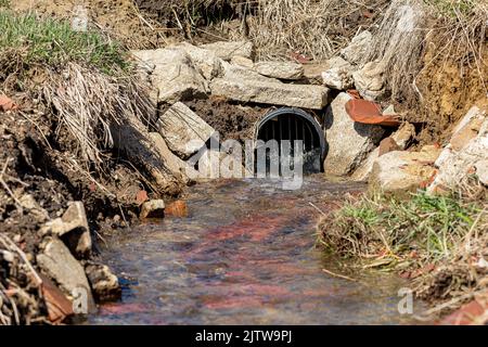 Bauernhof Feld Fliesenauslass mit Wasser fließt. Konzept der Wasserentwässerung, der Hochwasserkontrolle und der Wasserverschmutzung in der Landwirtschaft Stockfoto