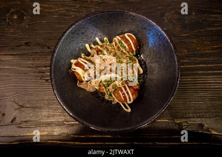 Selektive Konzentration auf Takoyaki- oder japanische Krake-Kugeln, serviert auf weißem Teller auf Holztheke im japanischen Restaurant. Stockfoto