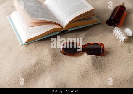 Buch, Sonnenbrille und Sonnencreme am Strand Stockfoto