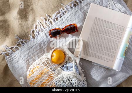 Beutel mit Orangen, Sonnenbrillen und Zeitschriften am Strand Stockfoto