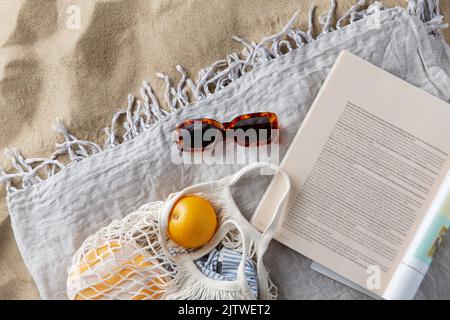 Beutel mit Orangen, Sonnenbrillen und Zeitschriften am Strand Stockfoto