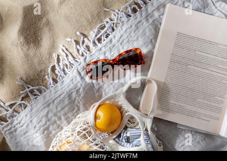 Beutel mit Orangen, Sonnenbrillen und Zeitschriften am Strand Stockfoto