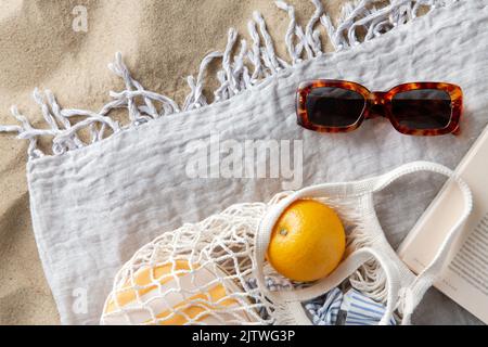 Beutel mit Orangen, Sonnenbrillen und Zeitschriften am Strand Stockfoto