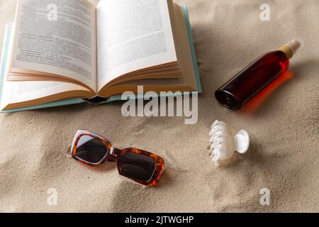 Buch, Sonnenbrille und Sonnencreme am Strand Stockfoto