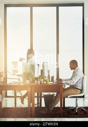Konzentriert sich auf seine Arbeit. Ein Geschäftsmann, der im Büro arbeitet, während ein Kollege vorbei kommt. Stockfoto