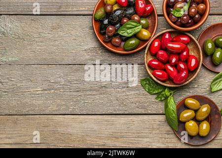 Teller mit verschiedenen Arten von leckeren Oliven auf Holzboden Stockfoto