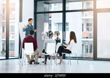 Unser nächster Schritt sollte in Richtung eines größeren Erfolgs gehen: Ein Geschäftsmann, der seinen Kollegen in einem modernen Büro eine Präsentation gibt. Stockfoto