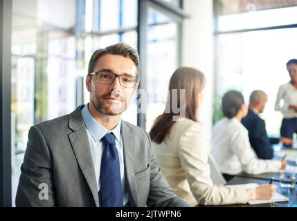 Hören Sie nie auf, Ihre Fähigkeiten und Stärken zu verbessern. Porträt eines reifen Geschäftsmannes, der in einem Sitzungssaal mit Kollegen sitzt. Stockfoto