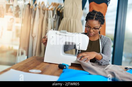 Eine junge Modedesignerin, die in ihrer Werkstatt eine Nähmaschine benutzt. Stockfoto