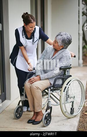 Ich danke Ihnen für Ihre Unterstützung. Eine ältere Frau im Rollstuhl, die von einer Krankenschwester in einem Altersheim für Sie da ist. Stockfoto