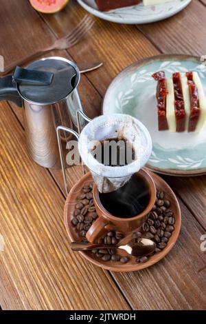 Wischen Sie den Kaffeefilter über die Tasse und die Kaffeebohnen. Im Hintergrund Guava süß und Quark. Stockfoto