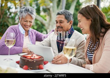 Hast du dieses Video gesehen, das ich gepostet habe? Ein älterer Mann, der seiner Familie etwas auf seinem Tablet zeigt, während sie draußen zu Mittag essen. Stockfoto
