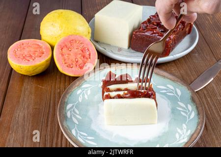 Mann, der mit einer Gabel aufhob, übereinander geschichtete Scheiben Guava-Süß- und Quark. Stockfoto