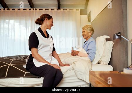 Und wie fühlen Sie sich heute. Eine Krankenschwester, die mit ihrer älteren Patientin in ihrem Zimmer sitzt. Stockfoto