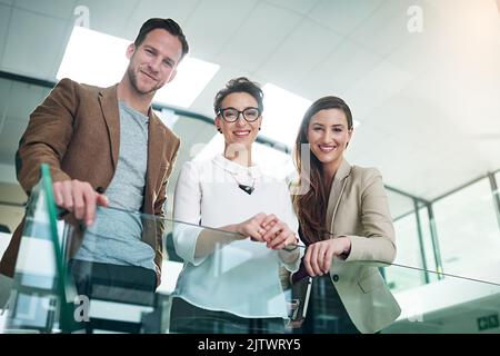 Kümmerte sich um Geschäfte. Porträt einer Gruppe von Kollegen, die sich in einem großen, modernen Büro auf einem Geländer stützen. Stockfoto