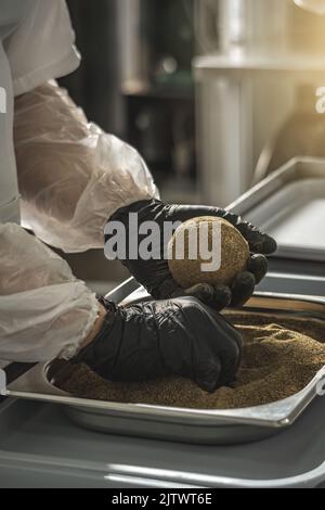 Ein Bauer in schwarzen Handschuhen streut schwarzen Pfeffer auf eine Käsebulle. Der Herstellungsprozess von würzigem Belper knolle Käse Stockfoto