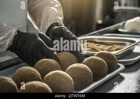 Ein Bauer in schwarzen Handschuhen streut schwarzen Pfeffer auf eine Käsebulle. Der Herstellungsprozess von würzigem Belper knolle Käse Stockfoto