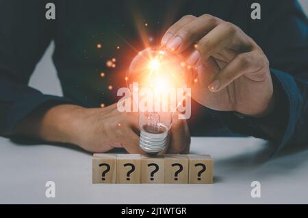 Kreativer Erfolg Idee Inspiration Geschäftskonzept Innovation Lösung auf dem Schreibtisch befindet sich eine Hand, die eine Glühbirne und ein Fragezeichen für einen Holzwürfelblock hält Stockfoto