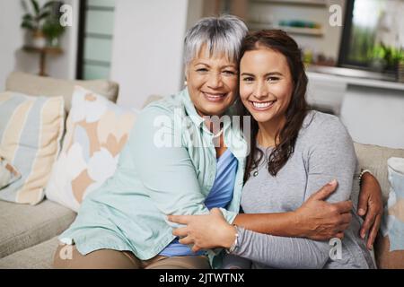 Nie zu alt für eine Umarmung von Mama. Beschnittenes Porträt einer Mutter und ihrer erwachsenen Tochter, die sich im Wohnzimmer umarmen. Stockfoto