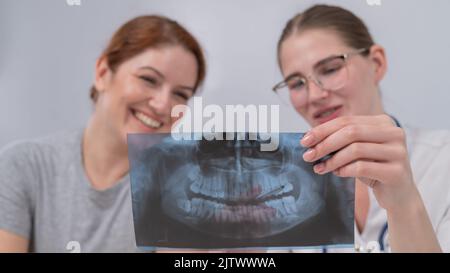 Eine Ärztin und ein Patient an der Rezeption diskutieren über eine Röntgenaufnahme des Kiefers. Stockfoto