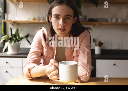 Porträt einer nicht-binären Trans-Frau, die zu Hause eine Kaffeetasse in der Küche hält Stockfoto