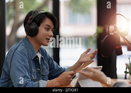 Asiatischer Podcaster, der Audio-Podcast macht und mit Gästen im Heimstudio zusammenarbeitet Stockfoto