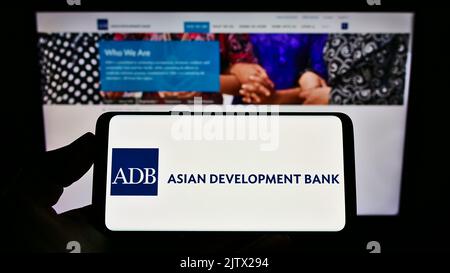 Person, die das Smartphone mit dem Logo der Organisation Asian Development Bank (ADB) auf dem Bildschirm vor der Website hält. Konzentrieren Sie sich auf die Telefonanzeige. Stockfoto