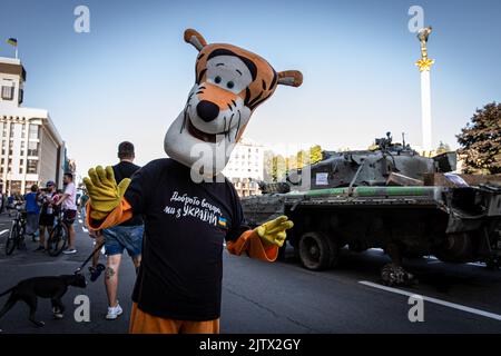 Kiew, Ukraine. 24. August 2022. Ein Mann, der sich wie die Zeichentrickfigur „Tigger“ verkleidet hat, die auf den Straßen in Kiew, Ukraine, zu sehen ist, während die Menschen auf den Straßen die abgerissenen russischen Panzer sehen. Während des Unabhängigkeitstages der Ukraine und fast 6 Monate nach der umfassenden Invasion der Ukraine am 24. Februar hält die Hauptstadt Kiew in der Hauptstraße der Chreschajtk-Straße eine Ausstellung ab, in der mehrere zerstörte militärische Ausrüstungen, Panzer und Waffen der Streitkräfte der Russischen Föderation (AFRF) gezeigt werden. (Foto von Alex Chan Tsz Yuk/SOPA Images/Sipa USA) Quelle: SIPA USA/Alamy Live News Stockfoto