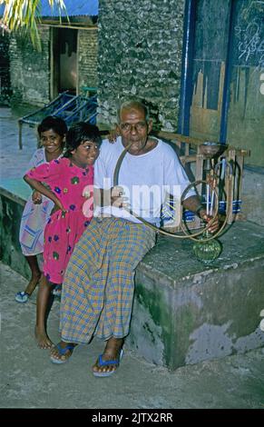 Junge Mädchen mit einem alten maledivischen Mann, raucht eine Wasserpfeife, Heimatinsel Mahembadhoo, Malediven, Indischer Ozean, Asien Stockfoto