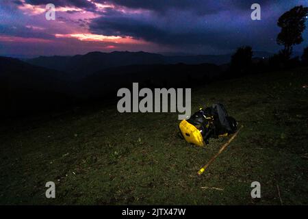 März 3. 2021 Uttarakhand Indien. Ein Rucksack und ein Spazierstock auf einem Hügel mit einer bunten Landschaft im Hintergrund während des Sonnenuntergangs. Himalaya TR Stockfoto