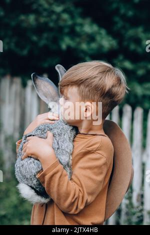 Ein Kind trägt ein graues Kaninchen in den Armen. Draußen Stockfoto