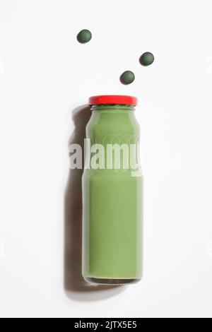 Grüner Smoothie in der Flasche und Spirulina-Algenpillen auf weißem Hintergrund. Nützliche Gewohnheiten, Selbstpflege und gesundes Lifestyle-Konzept. Gesunder Snack. Stockfoto