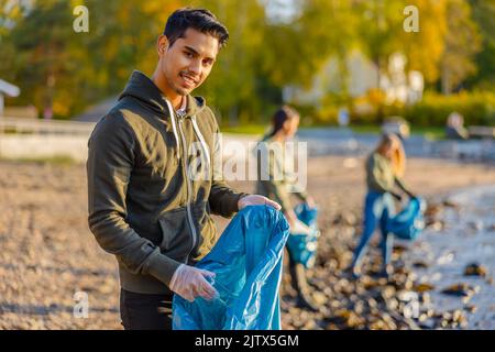 Mann sammelt Müll in der Tasche mit einer Gruppe von Freiwilligen an sonnigen Tag Stockfoto