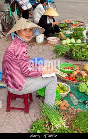 Vietnamesische Dame mit Bambushut, die Gemüse auf dem Straßenmarkt in Hai Phong, Vietnam verkauft Stockfoto