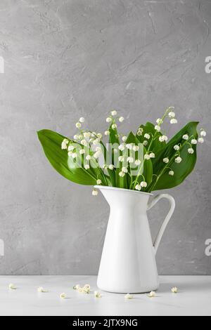 Stillleben mit Maiglöckchen Blumenstrauß in Vase auf grauem Betongrund. Vertikale Ausrichtung. Hochzeitskonzept oder Urlaubskonzept Stockfoto