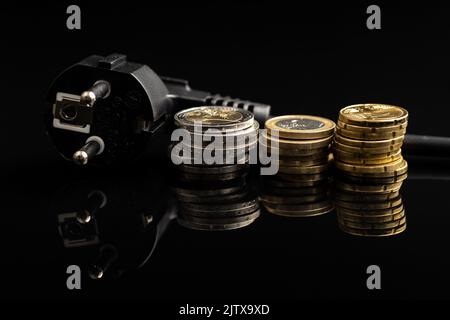 Schwarzer Stecker und Euro-Münzen auf schwarzem Hintergrund. Konzept der steigenden Strompreise. Stockfoto