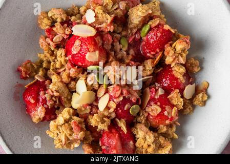 Nahaufnahme von köstlichen Erdbeerbröseln mit Mandeln und Kürbiskernen auf einem Teller. Draufsicht. Leckeres Frühstück Stockfoto