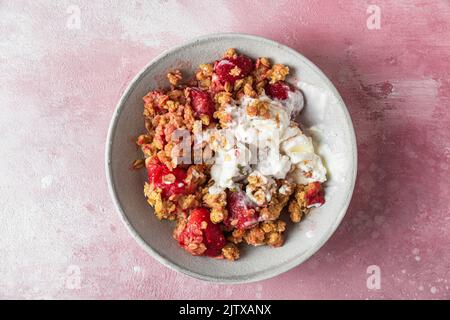 Köstliche Erdbeeren zerbröseln mit Eis, Mandeln und Kürbiskernen auf einem Teller auf rosafarbenem Hintergrund. Draufsicht. Leckeres Frühstück Stockfoto