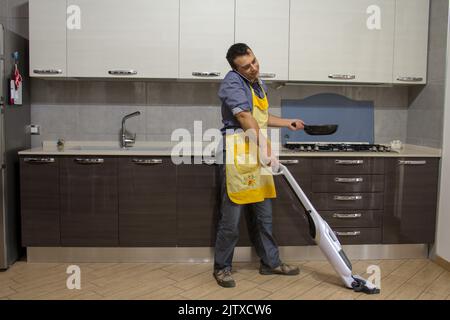 Junge, während sie am Telefon kochen und putzen. Neuer Mann des Hauses Stockfoto