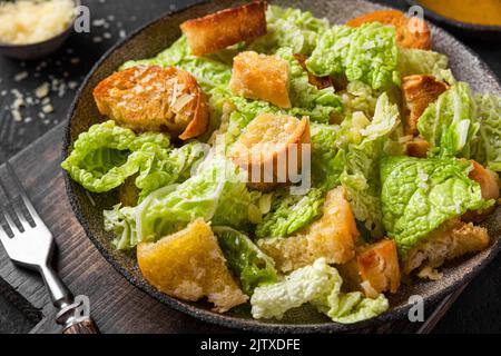 Klassischer Caesar-Salat mit knusprigen hausgemachten Croutons, Parmesan-Käse und caesar-Dressing auf einem Teller auf schwarzem Hintergrund Stockfoto