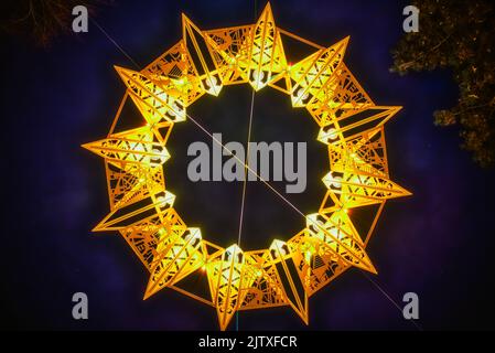Symmetrischer gelber Stern (TetradecagonGelber Stern (Tetradecagon oder vierzehnseitiges Polygon) aus hellem Licht, das am Nachthimmel leuchtet. Tetrakaidekagon Stockfoto